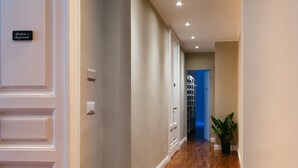 A hallway with a light switch, a door with a nameplate, and a blue door at the end. - Le 4 Leggende (Catania)