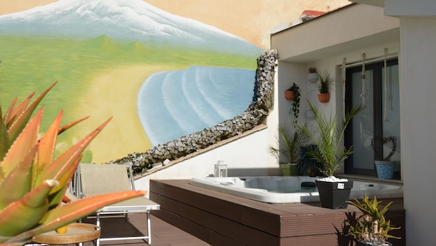 A modern outdoor area with a hot tub, potted plants, and a mural of a mountain. - Le 4 Leggende (Catania)
