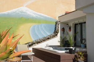 Una zona esterna moderna con una vasca idromassaggio, piante in vaso e un murale raffigurante una montagna.