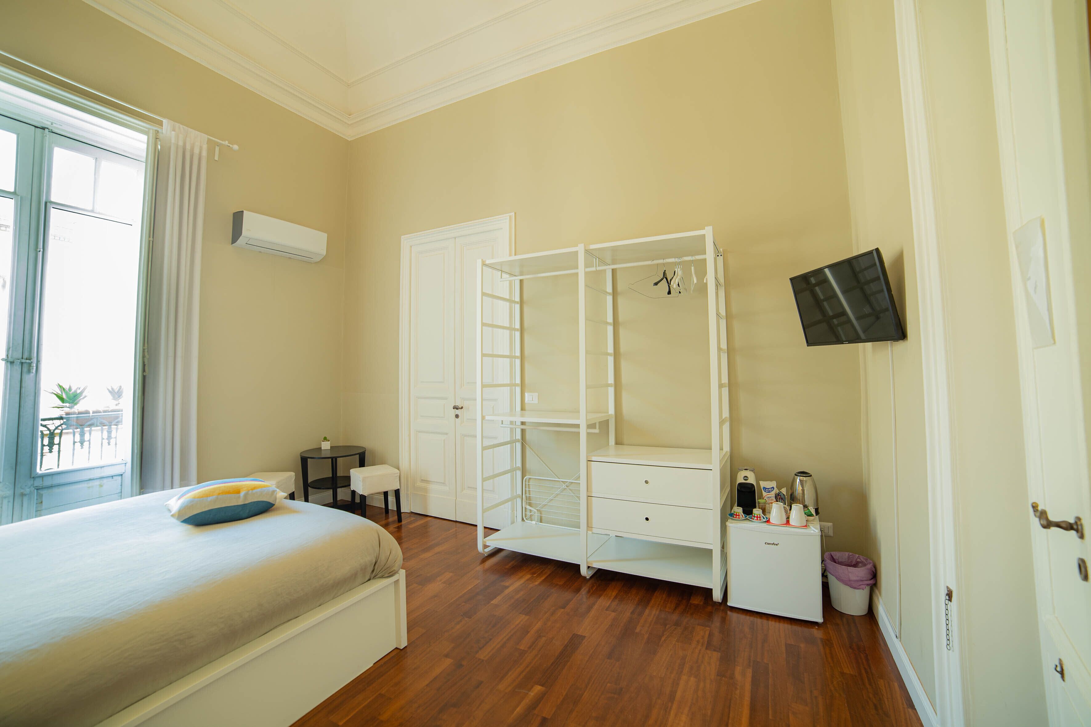 A bedroom with a bed, a wardrobe, a small table, and a trash bin.