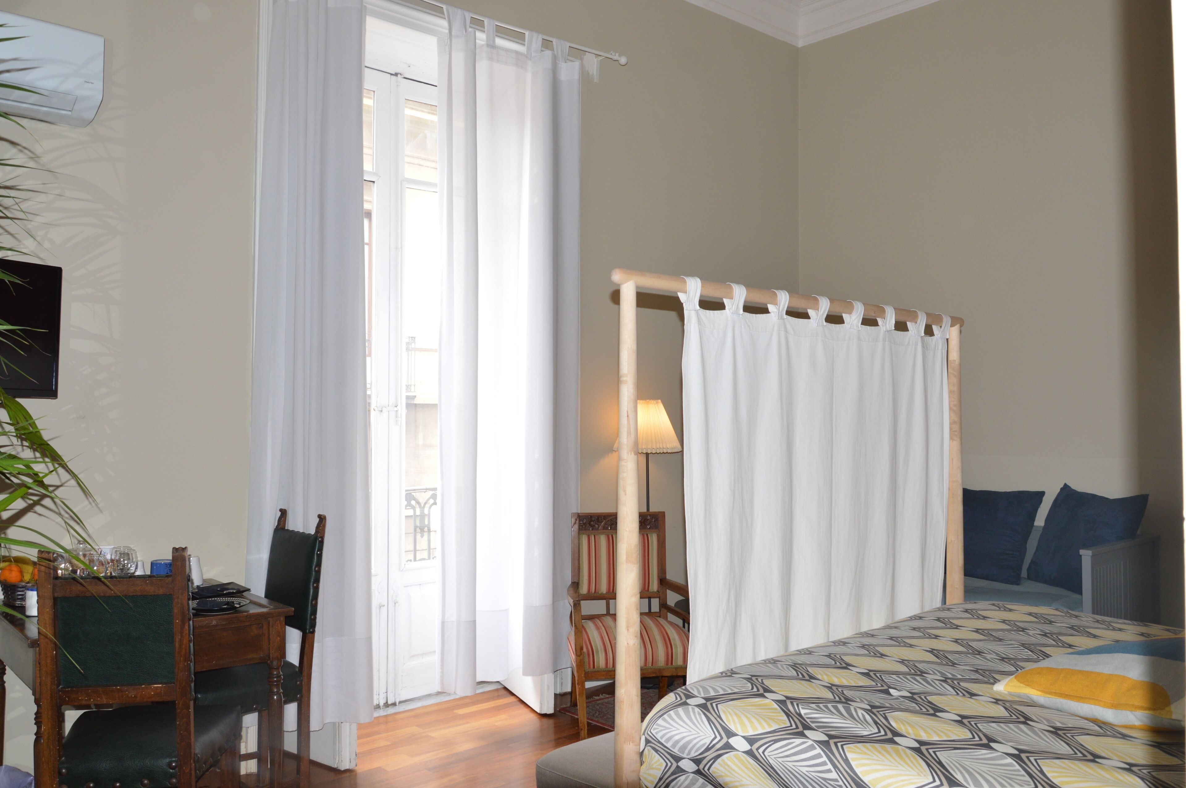A bedroom with a bed, a chair, a table, and a window with curtains.