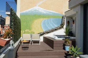 Eine Dachterrasse mit Wandgemälde einer Berglandschaft, einem Whirlpool und Sitzgelegenheiten im Freien.