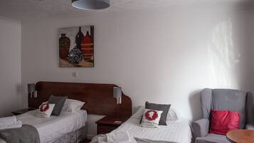Una camera d'albergo con due letti, una testiera in legno, un quadro appeso e una poltrona grigia.