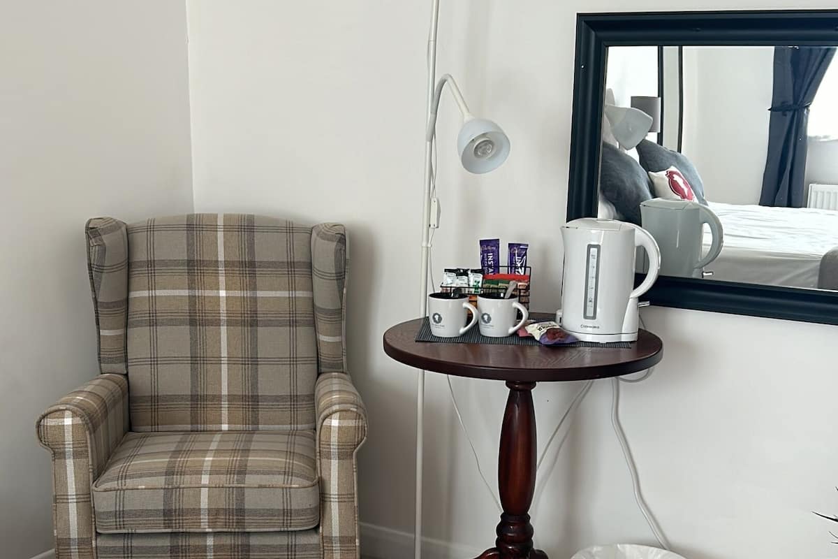A plaid armchair, a small round table with a lamp, a coffee maker, and a white bucket.