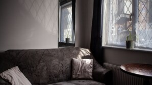 A dark-colored sofa with two cushions, a small table, and a window with a potted plant. - Oliver Twist Country Inn (Wisbech)