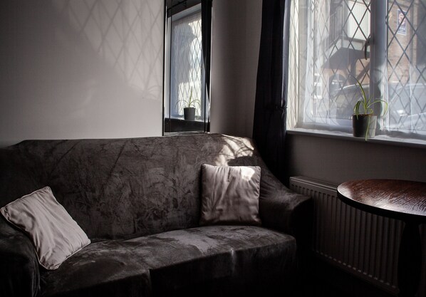 A dark-colored sofa with two cushions, a small table, and a window with a potted plant. - Oliver Twist Country Inn (Wisbech)