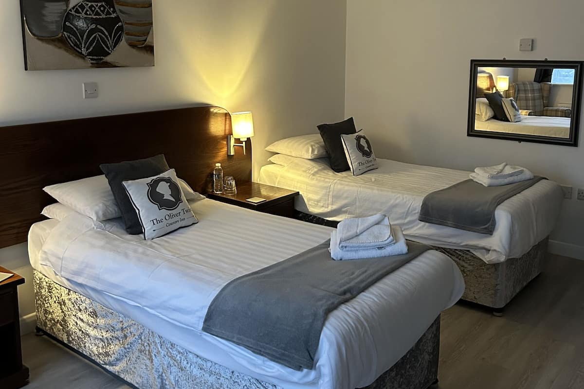 A hotel room with two beds, a headboard, bedside lamps, a mirror, and a painting on the wall.