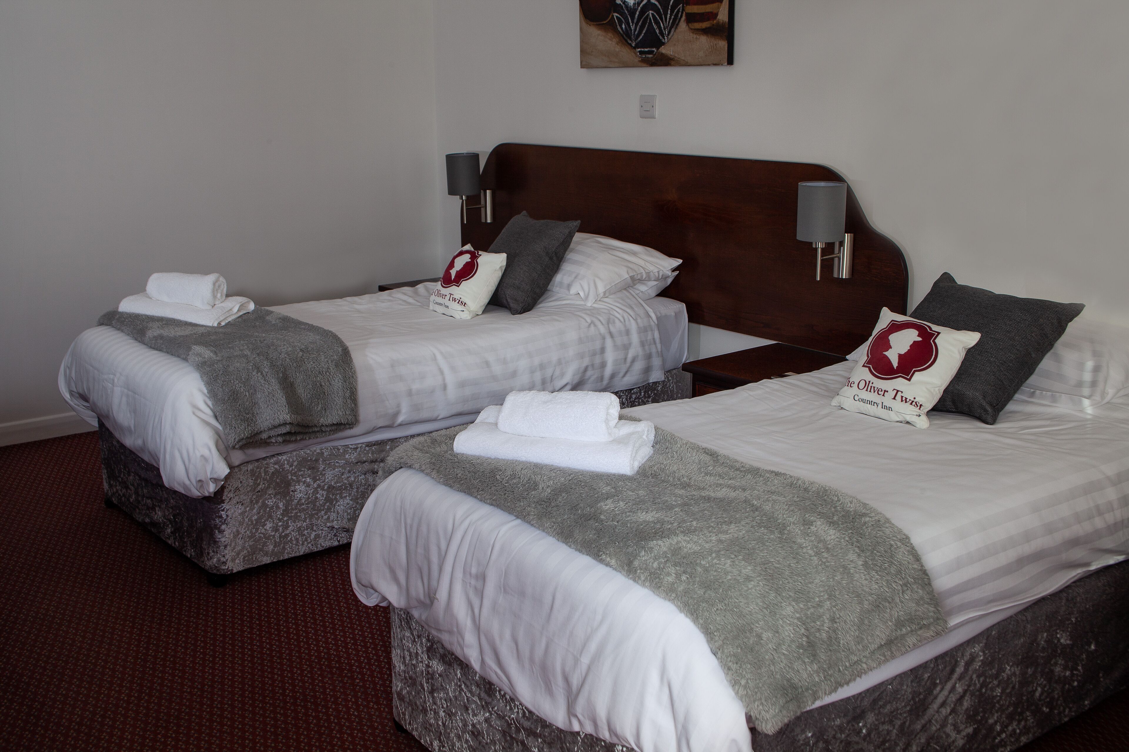 Two twin beds with white linens, grey throw blankets, and pillows with a red logo.