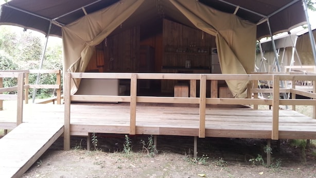A wooden cabin with a covered deck and a ramp leading to the entrance. - Camping BelleRive (Montfrin)