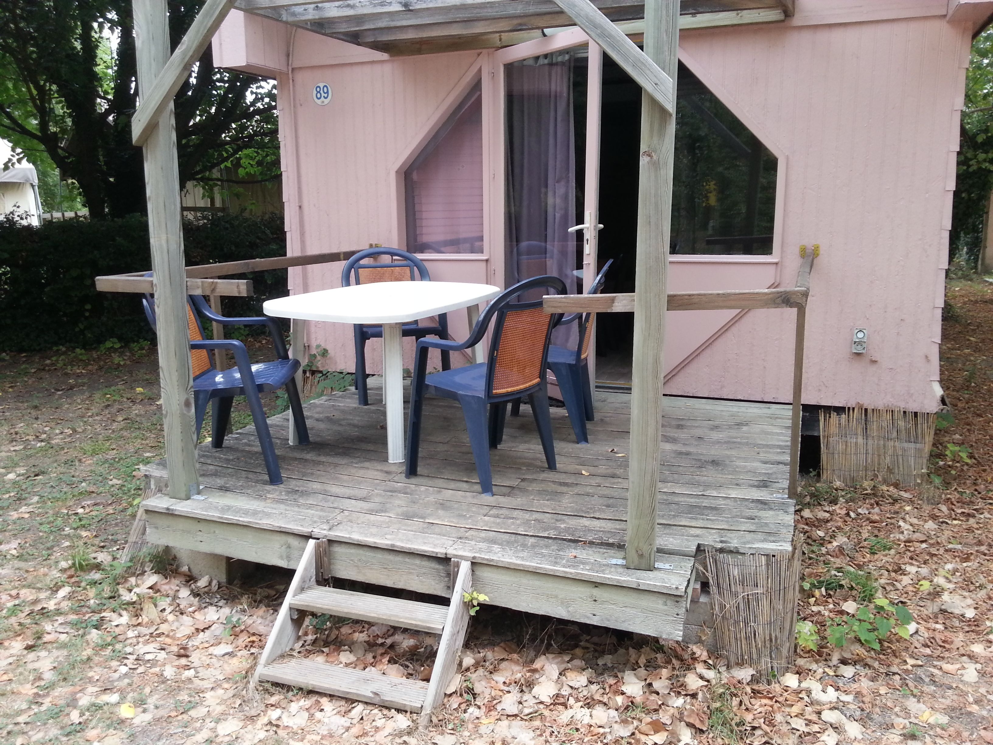 A small wooden structure with a table and chairs, a number '89' on the wall, and a covered entrance.