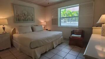 A bedroom with a bed, a ceiling fan, a window with a view, and a small table with a lamp.