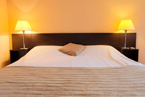 A neatly made bed with a headboard, two bedside lamps, and a single pillow.