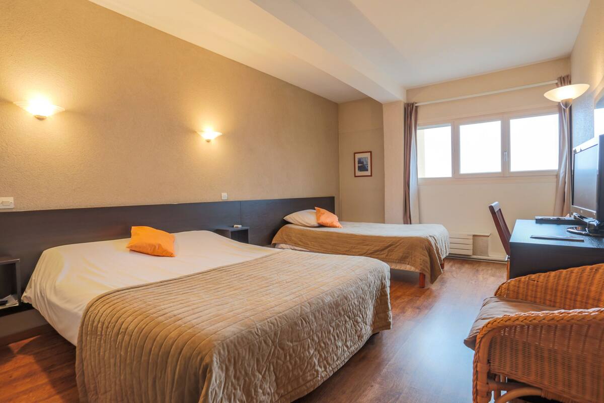 A hotel room with two beds, a desk, a chair, and a window with curtains.
