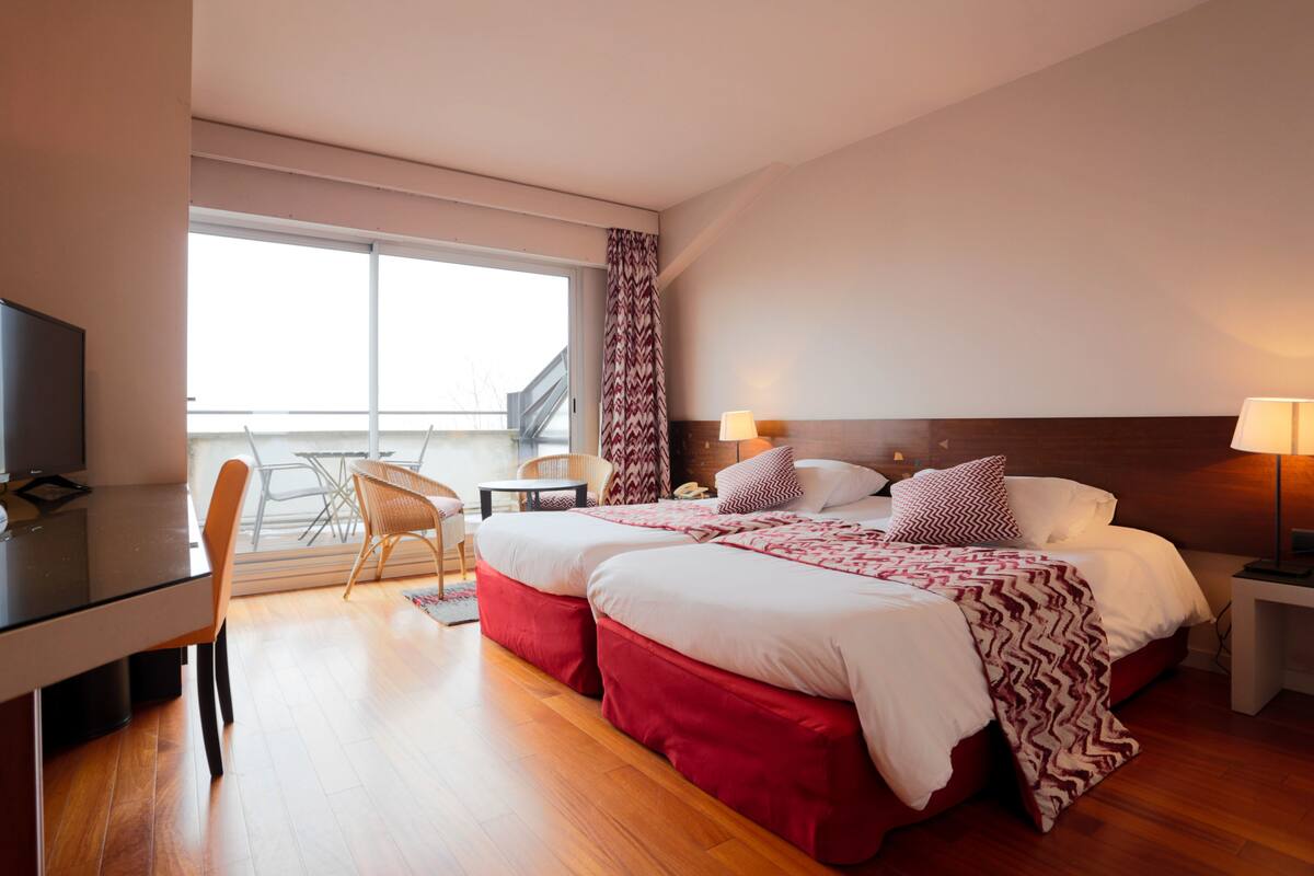 A hotel room with a bed, bedside tables, a desk, and a chair.