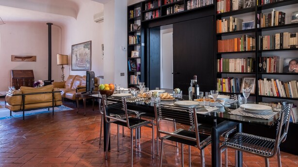 A dining area with a table set for four, surrounded by bookshelves filled with books. - Santo Spirito Apartment (Florence)