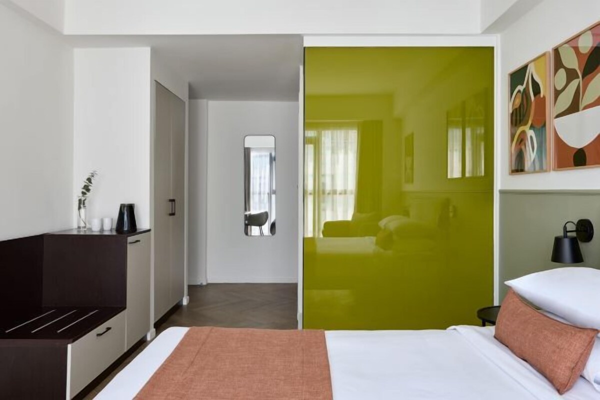 A hotel room with a bed, a desk, and a mirror.