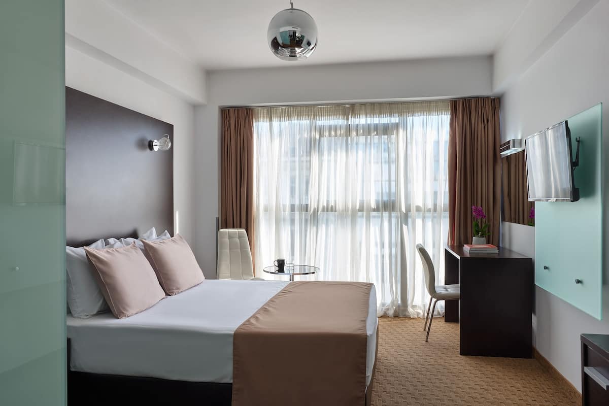 A hotel room with a bed, a desk, a chair, a TV, and a window with curtains.