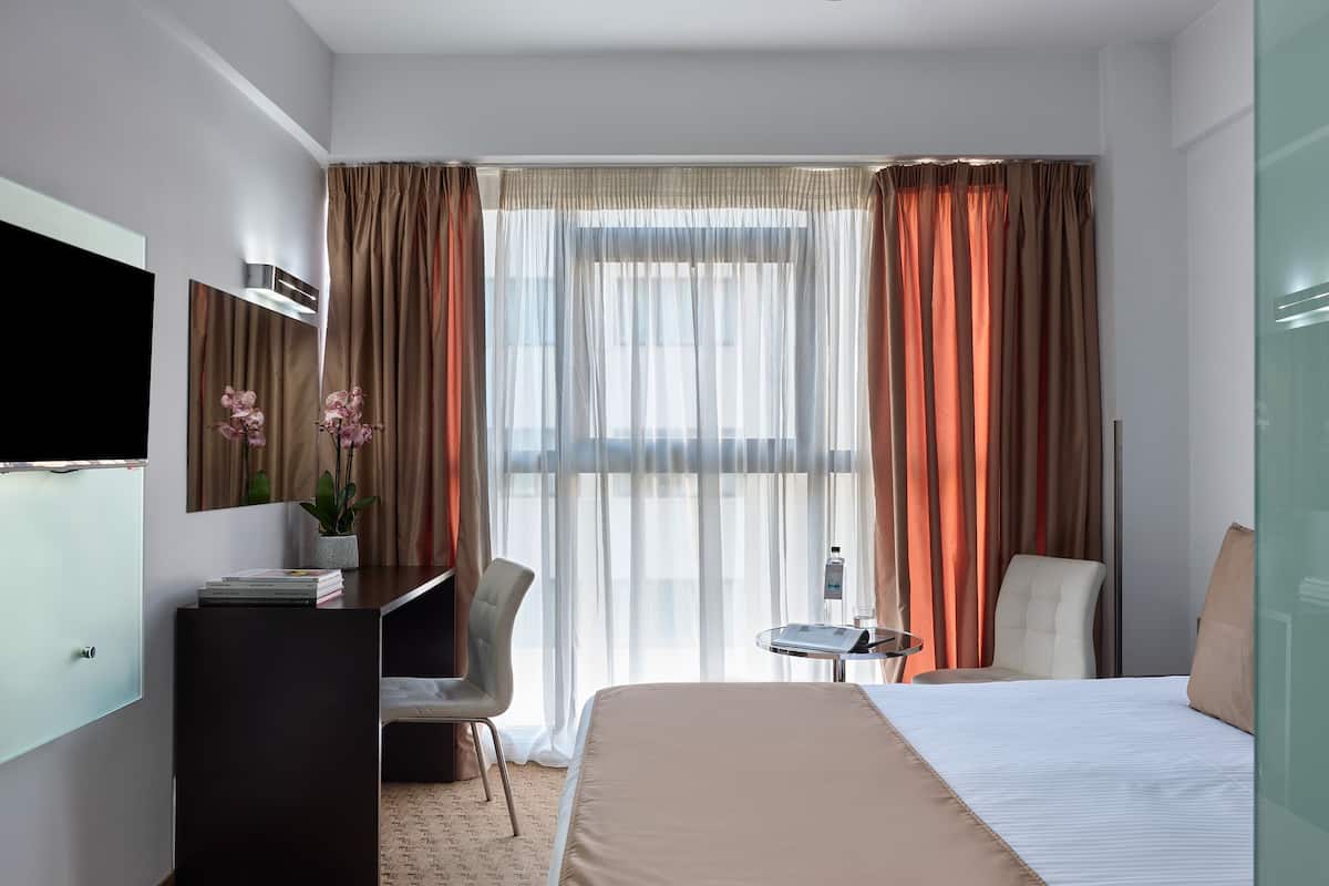 A hotel room with a bed, a desk with a chair, a TV, and a small table with a bottle.