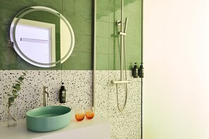 A bathroom with a round mirror, a sink with a green basin, a faucet, a showerhead, and a speckled backsplash. - Breeze Boutique Hotel (Athens)