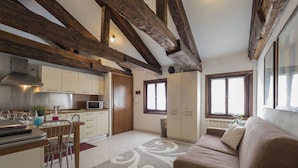 Una cocina moderna con gabinetes blancos, un microondas y un comedor con mesa y sillas. Hay un sofá marrón en la sala y una ventana con vistas.
