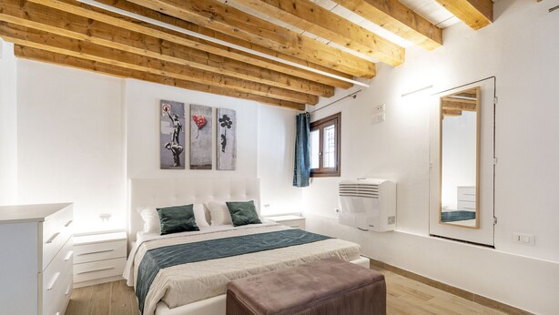 Un dormitorio con cama, mesitas de noche, un espejo y una ventana.