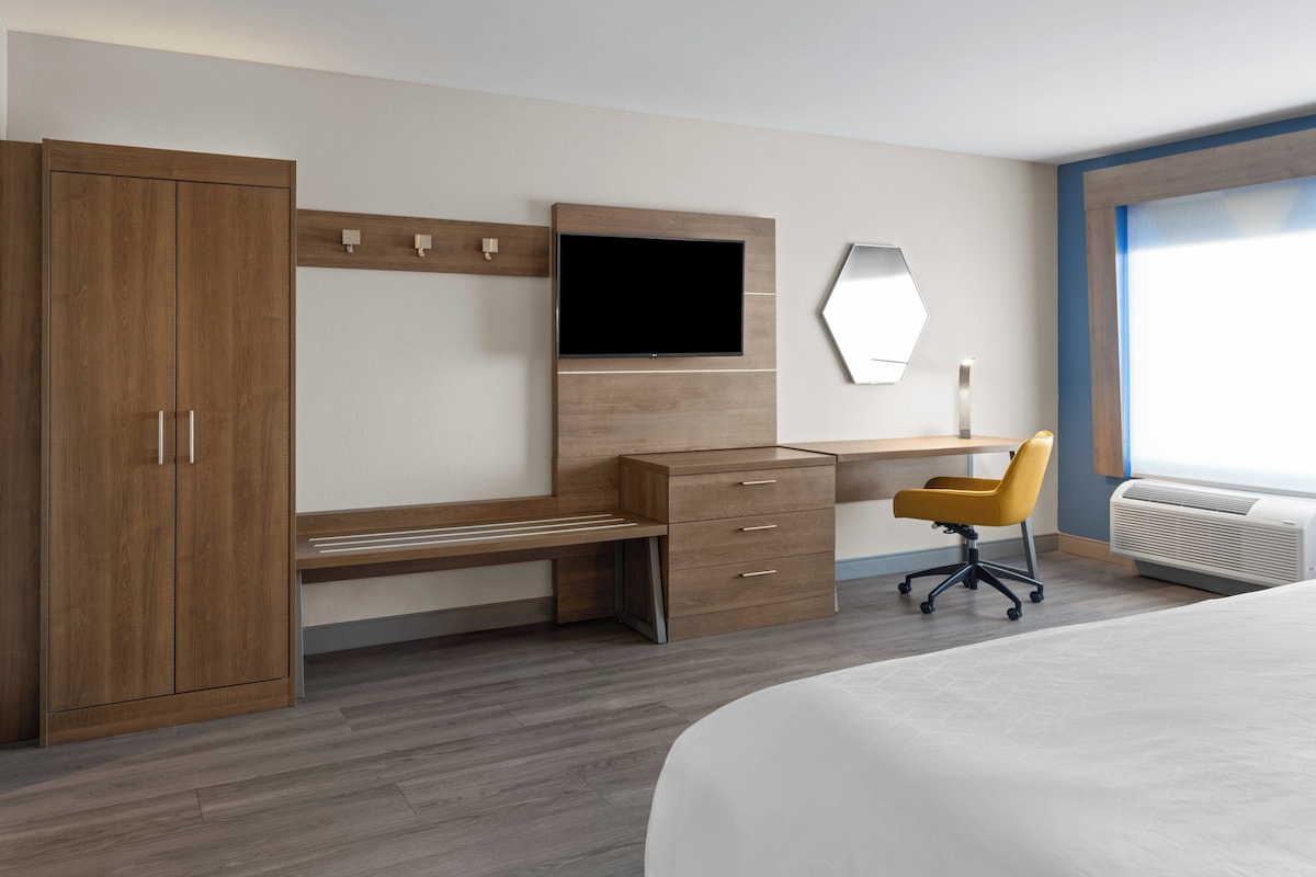 Une chambre d’hôtel moderne équipée d’un bureau en bois, d’un téléviseur à écran plat, d’un grand lit et d’un appareil de climatisation.