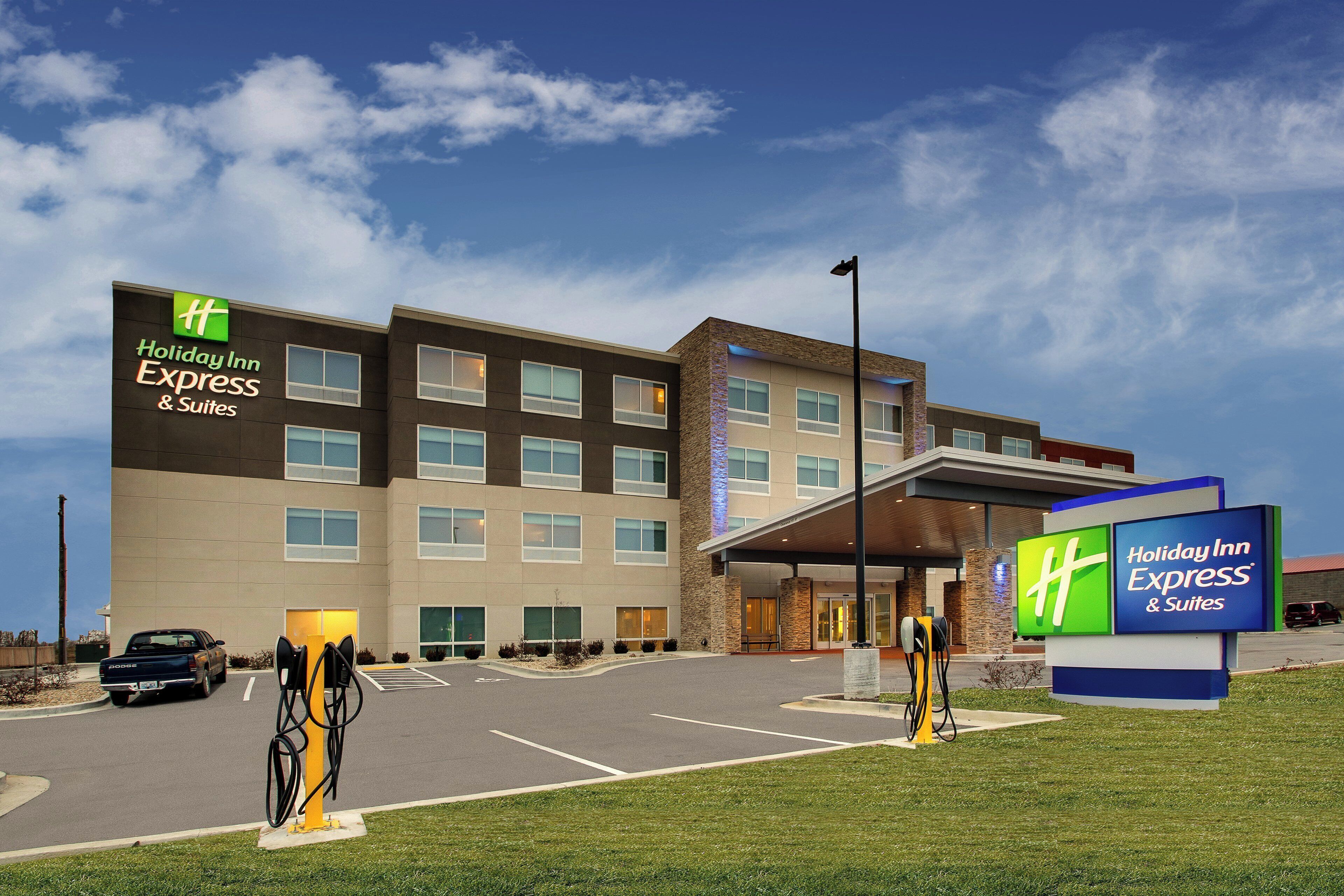 A Holiday Inn Express & Suites hotel with a parking lot, a fuel pump, and a clear sky.