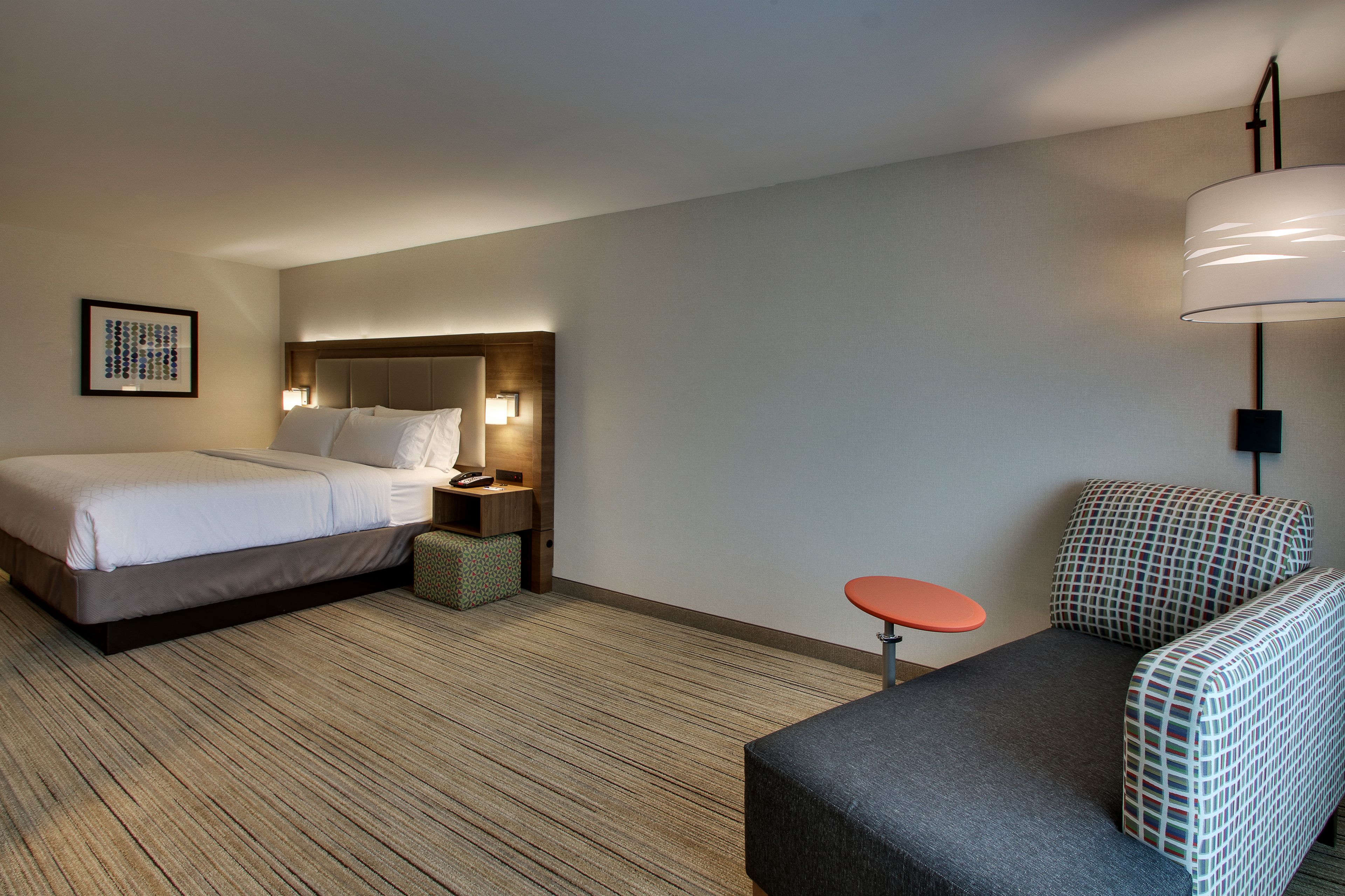 A hotel room with a bed, a small table, a sofa, a lamp, and a framed picture on the wall.