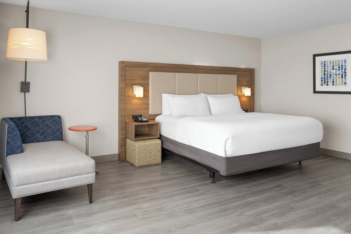 Une chambre d’hôtel avec un lit, une chaise, une petite table et une lampe fixée au mur.