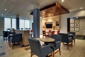 A modern indoor seating area with tables and chairs, a flat-screen TV mounted on the wall, and a patterned wall decoration. - Holiday Inn Express & Suites Mt Sterling North by IHG (Mount Sterling)