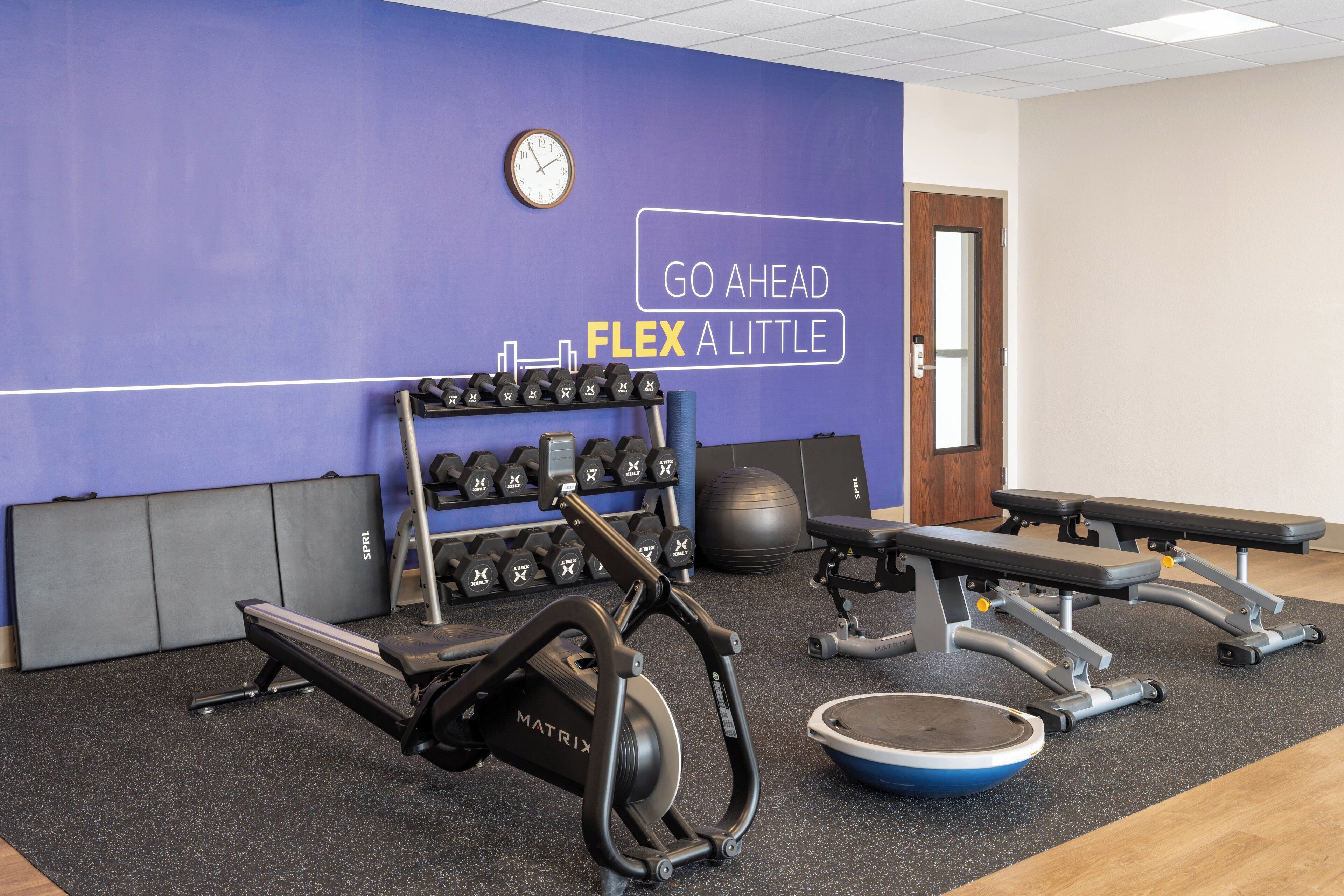 A gym with exercise equipment, a wall clock, and motivational text.