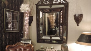 Una habitación con un sillón de cuero capitonado, una consola de madera oscura con objetos decorativos, un espejo grande y ornamentado, y una lámpara de pie.