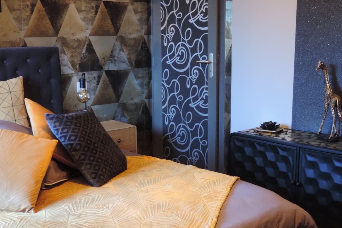 A bed with patterned bedding, a geometric wall design, a decorative cabinet with a giraffe figurine, and a wall with a swirl pattern.