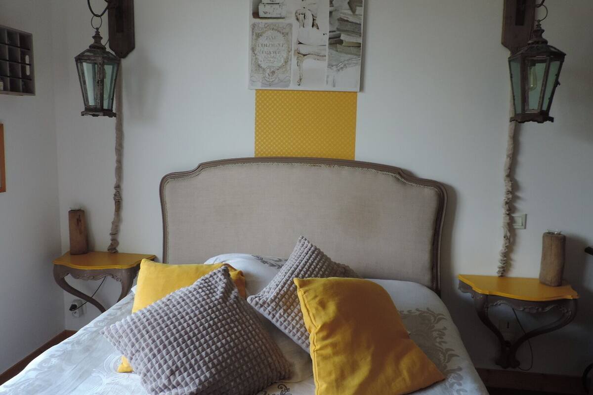 A bedroom with a bed, two nightstands, and a wall with a picture and two wall-mounted lanterns.