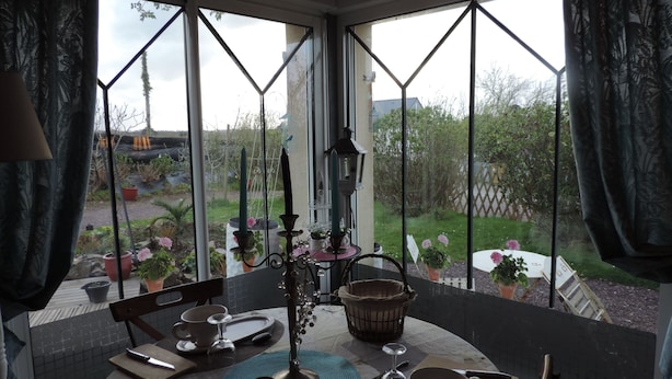 Comedor con una mesa dispuesta para dos, un centro de mesa con velas y vistas a un jardín a través de amplios ventanales.
