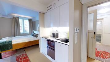 A compact hotel room with a bed, kitchenette, and a door leading to a hallway.