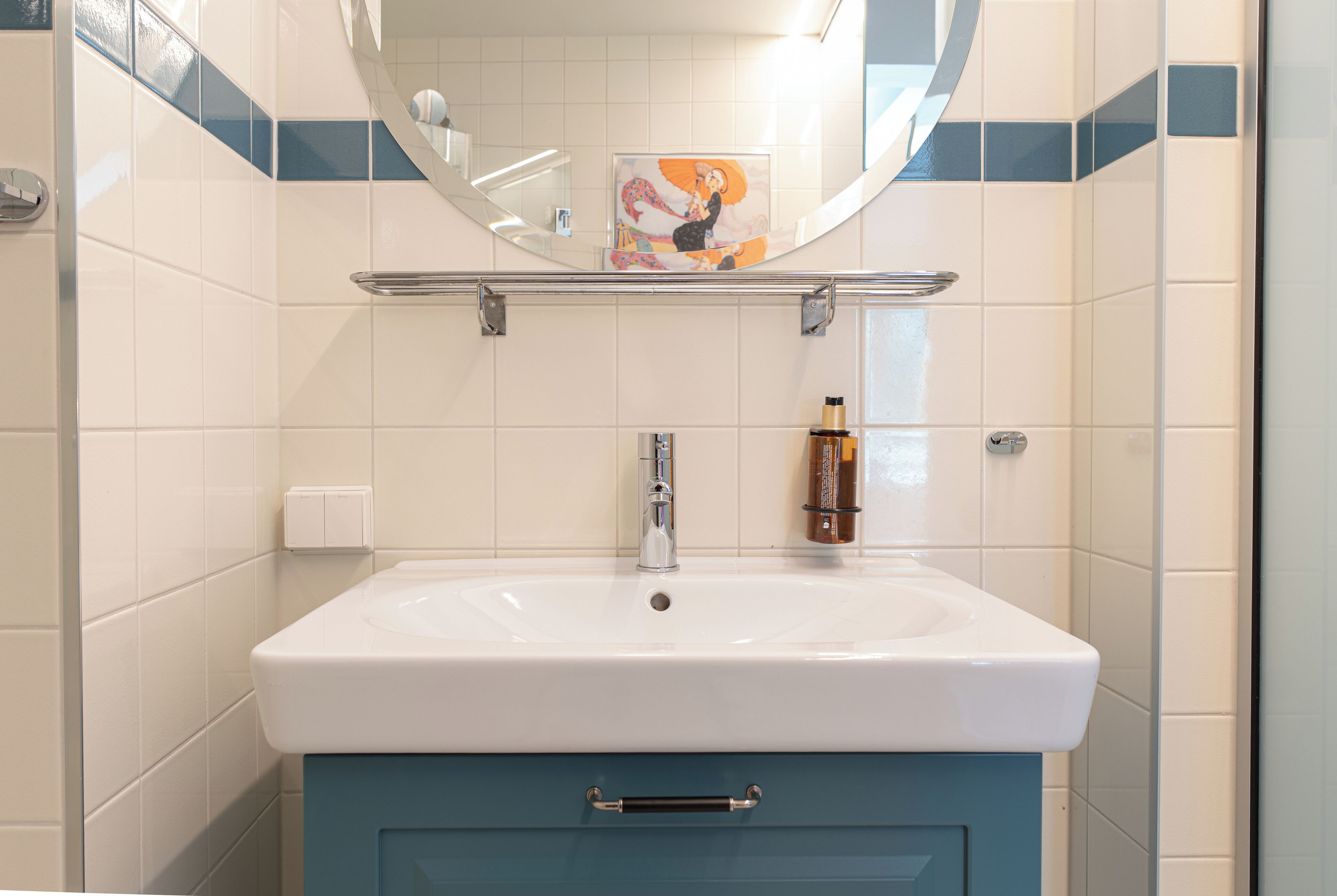 A bathroom with a white sink, blue cabinet, and a mirror above.