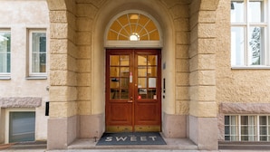 Entrada de un edificio con una puerta de madera doble, un ventanal arriba y un felpudo que dice 'THE SWEET'.
