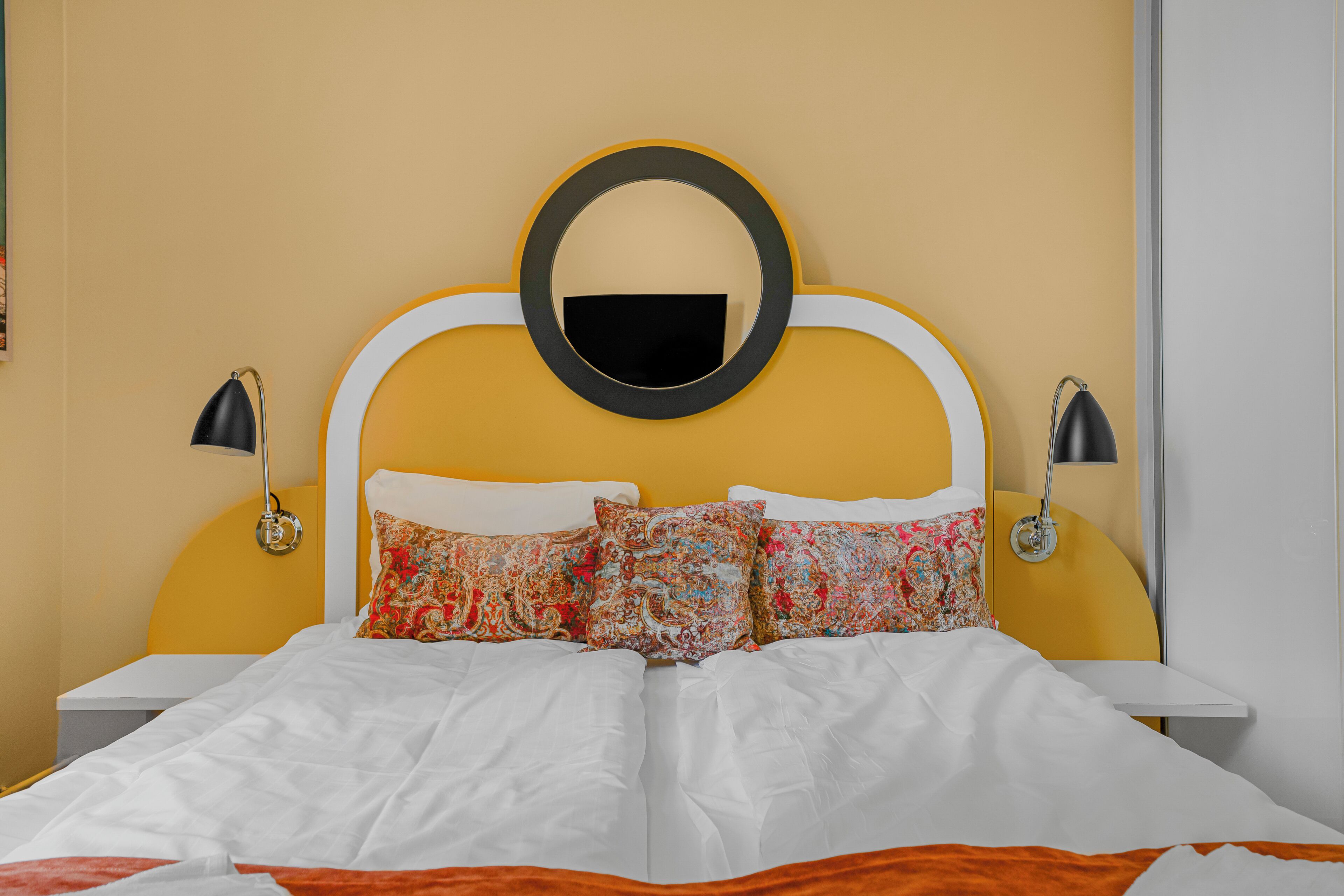Un lit avec une literie blanche, une tête de lit jaune et deux lampes de chevet.
