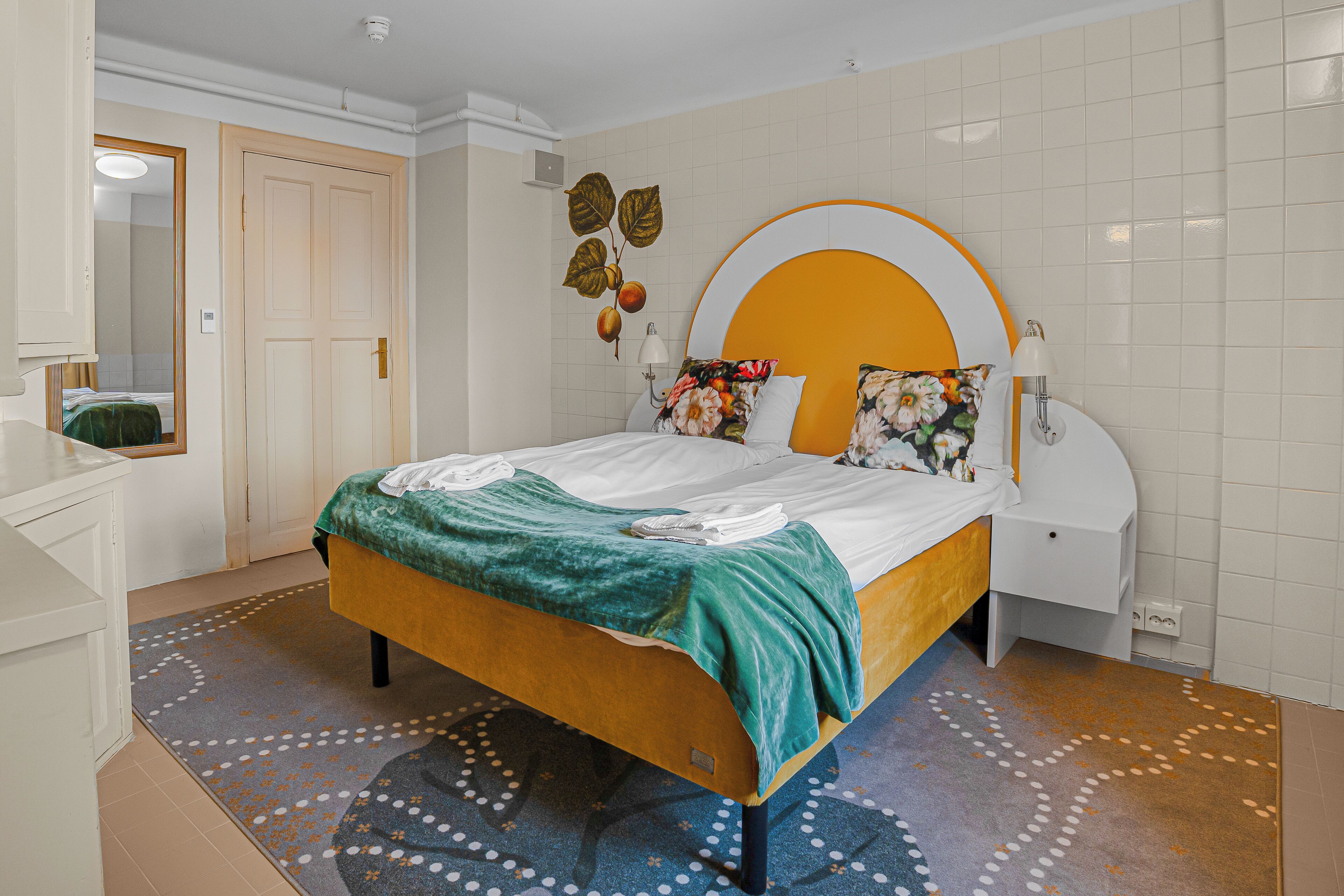 A bedroom with a bed, bedside tables, a dresser, a mirror, and a wall with a fruit design.