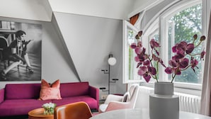 Una sala moderna con un sofá púrpura, una mesa redonda con un florero de orquídeas moradas y un ventanal con vistas a la vegetación.