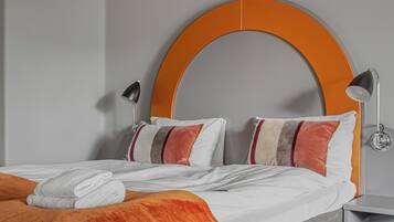 Una habitación de hotel moderna con una cama gris, cabecera naranja y mesita de noche gris.