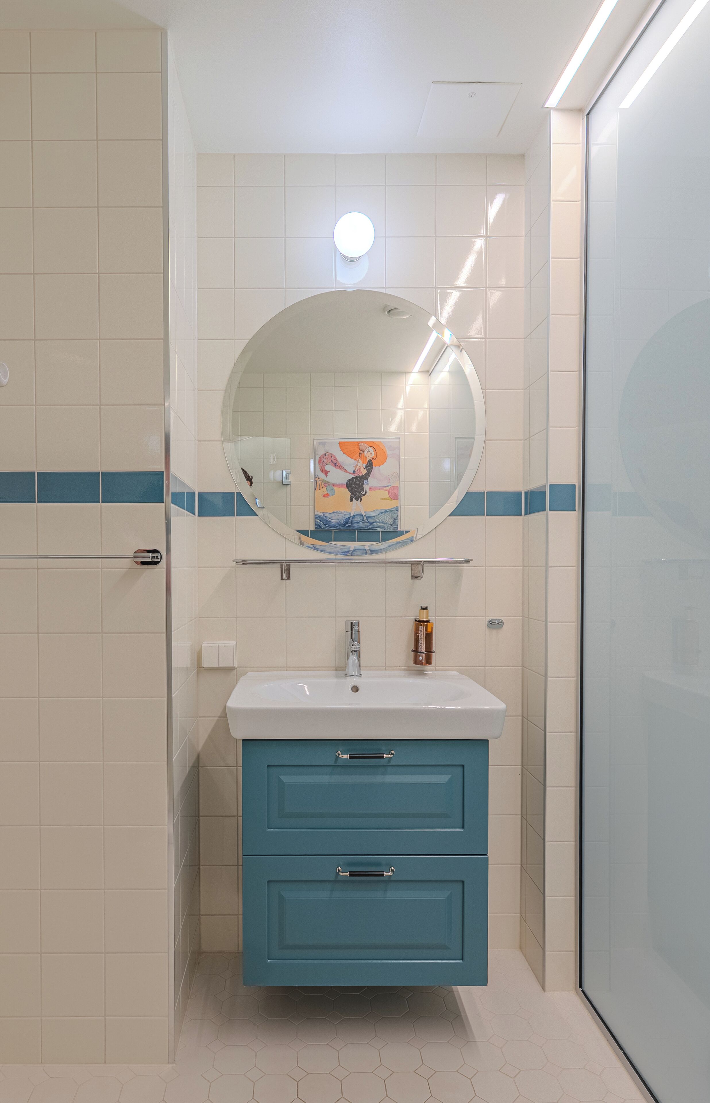 Une salle de bain avec un lavabo blanc, des meubles bleus et un miroir rond.