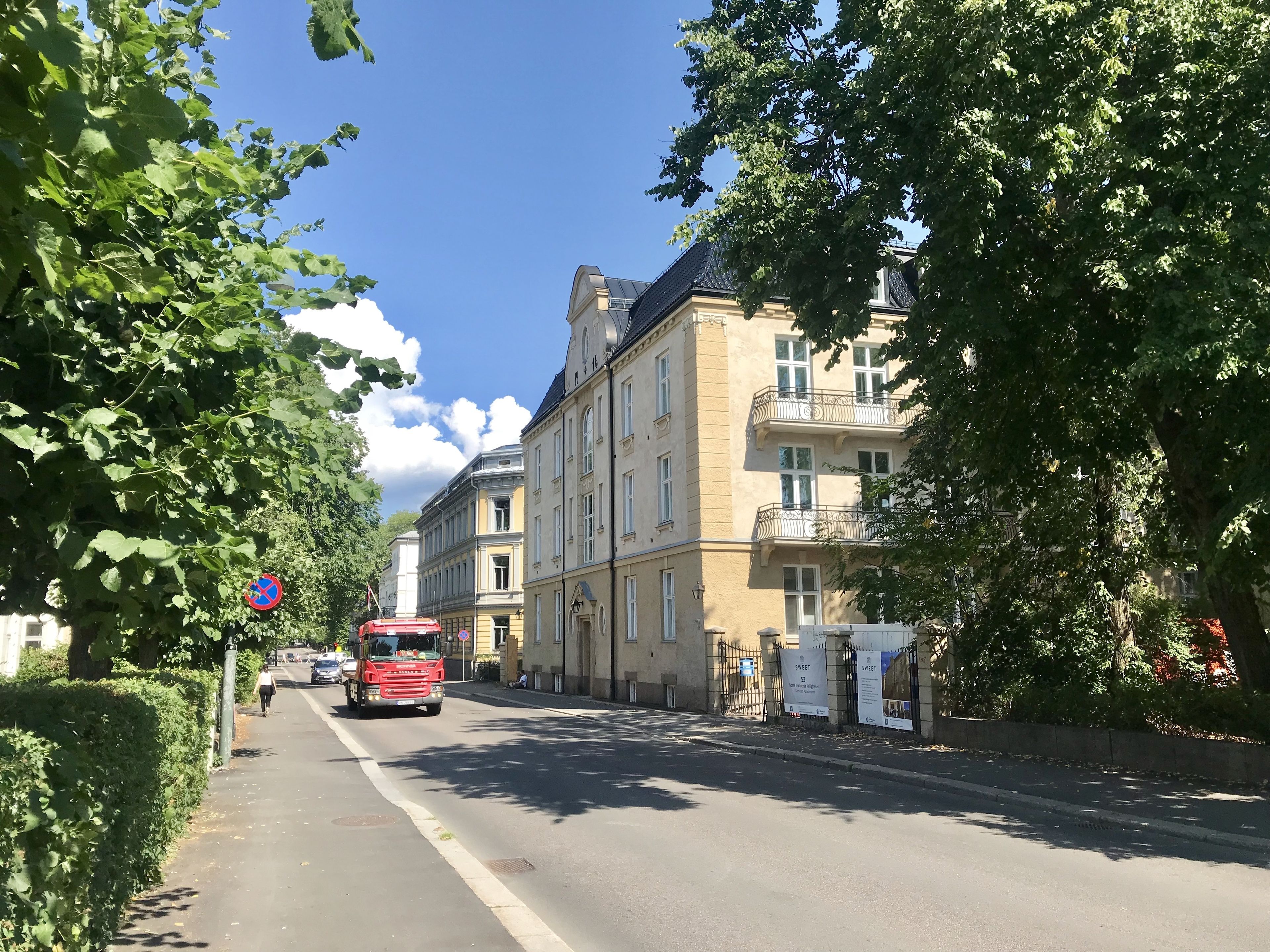 A street with buildings, a red truck, and a pedestrian.
