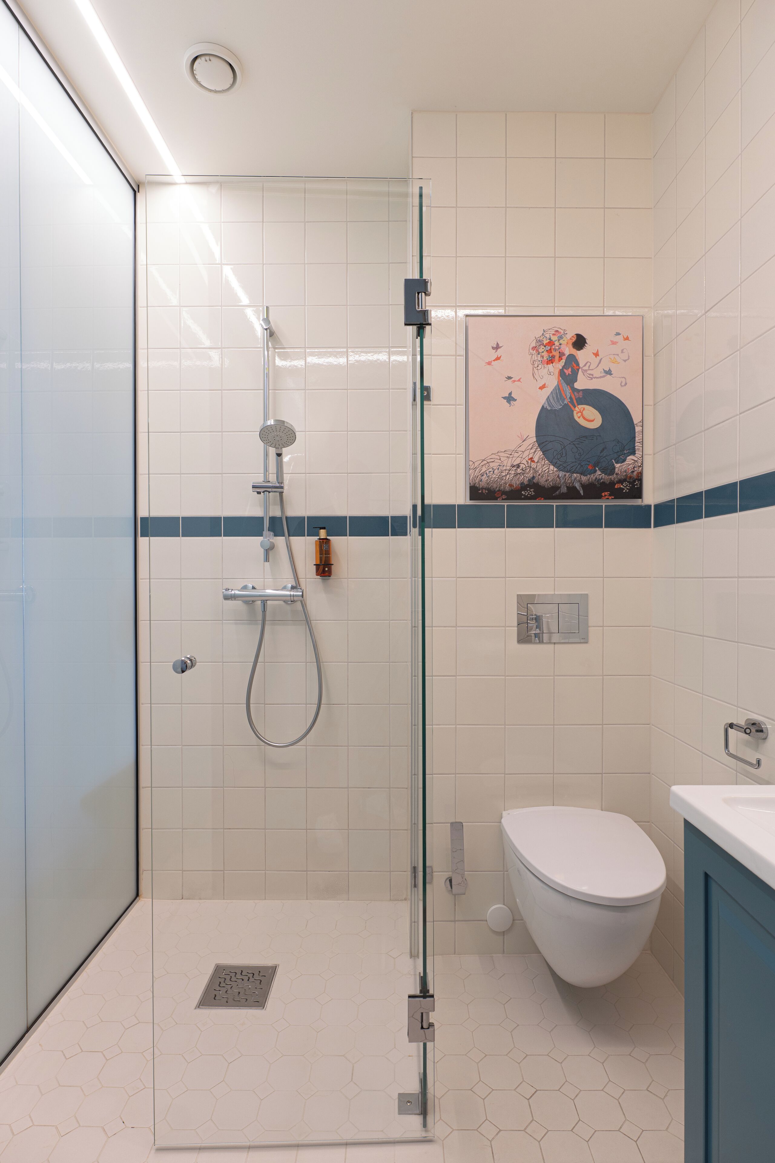 A modern bathroom with a glass shower enclosure, a white toilet, and a blue-tiled shower area.