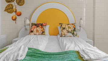 A hotel room with a bed, two pillows, a nightstand, a lamp, and a wall with a floral design.