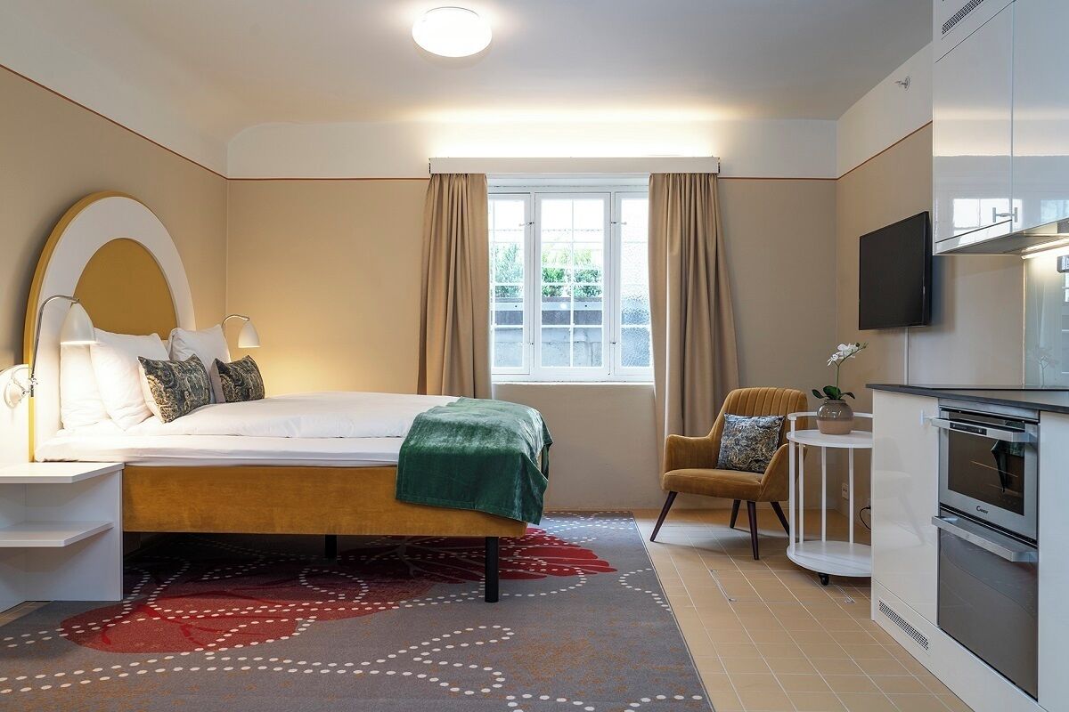 Een moderne hotelkamer met een bed, nachtkastje, televisie en kitchenette.