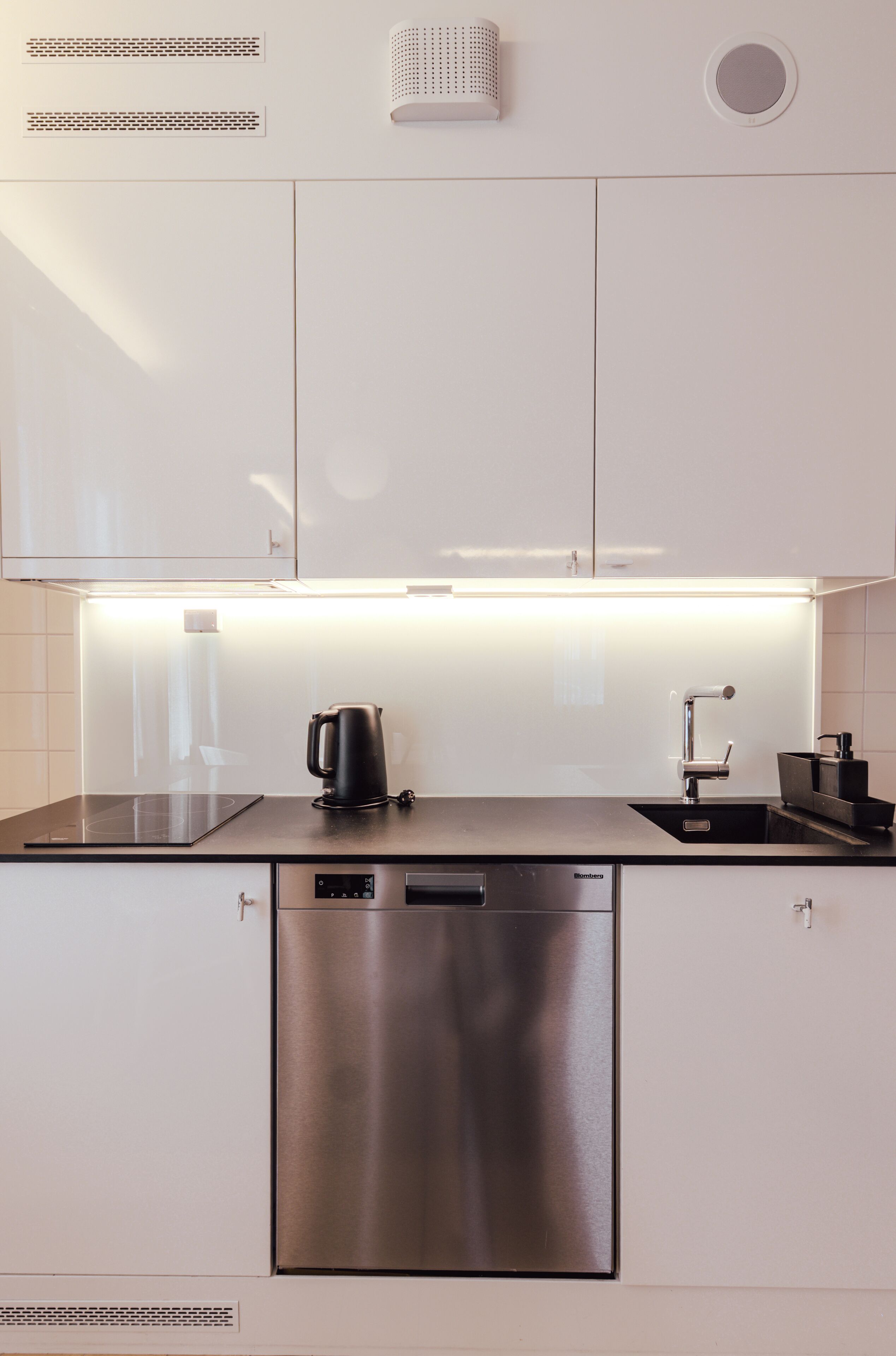 A modern kitchen with white cabinets, a stainless steel dishwasher, a kettle, and a sink.