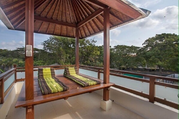 A wooden gazebo with a thatched roof overlooking a body of water and lush greenery.