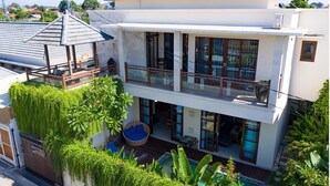 Ein zweistöckiges Haus mit Balkon, Pool und üppiger Bepflanzung.